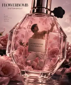 A shirtless male model posed inside a large faceted transparent perfume bottle surrounded by pink flowers, captured in a surreal luxury fragrance campaign setting.